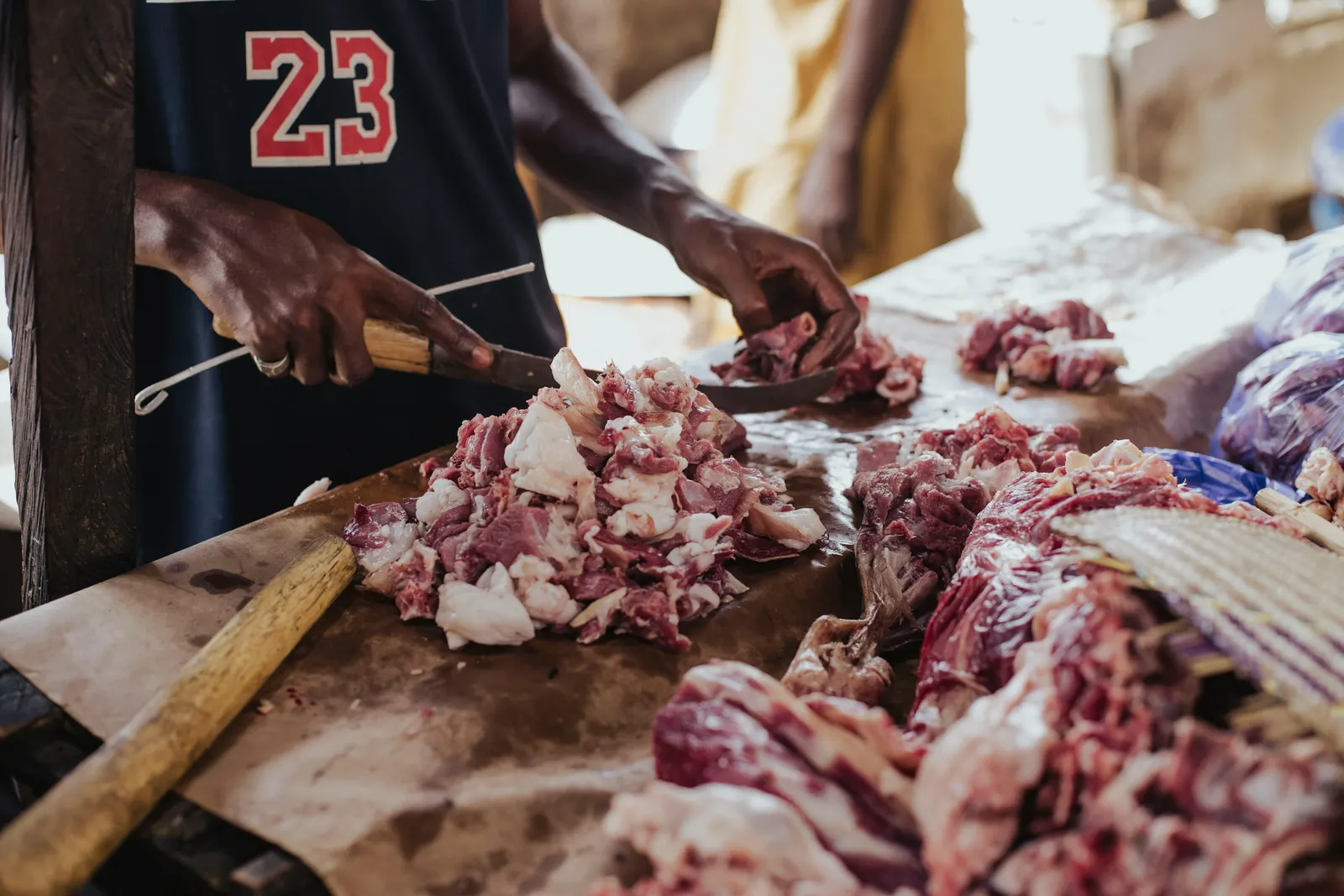 A butcher cutting fresh beef on a market table with a heavy cleaver, the cuts laid out in front