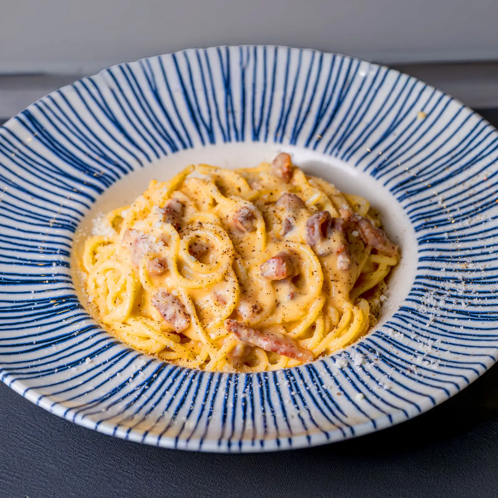A plate of spaghetti with pancetta and a creamy, pepper-flecked sauce, in the style of a Roman carbonara