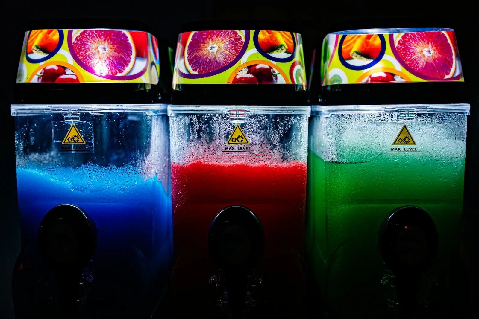 Three unbranded frozen drink machines glowing blue, red and green against a dark background