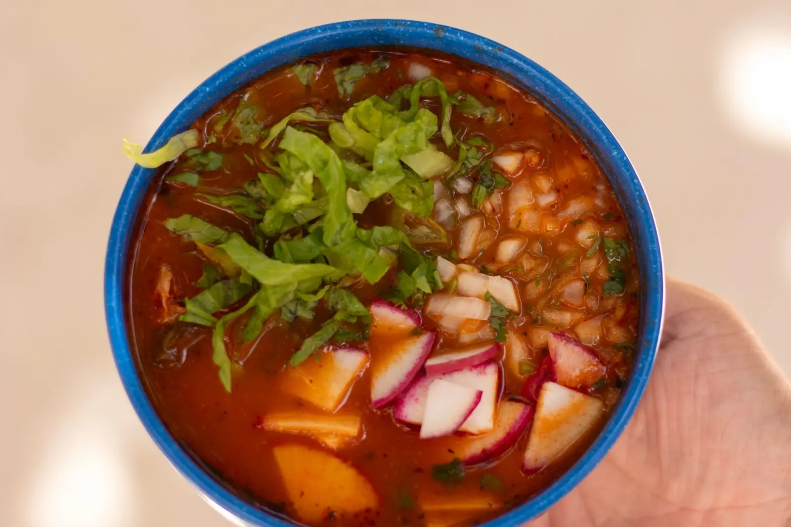 A blue bowl of Mexican pozole with broth, shredded meat and garnishes