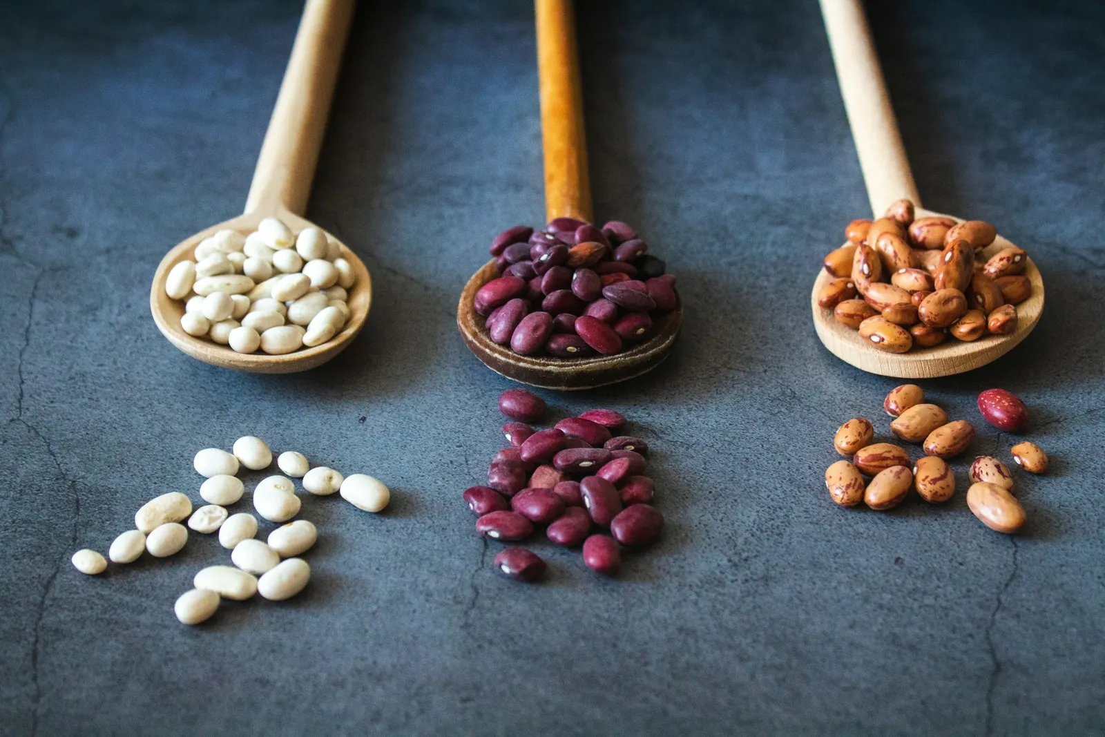 Dried red and brown beans with a wooden spoon on a dark surface