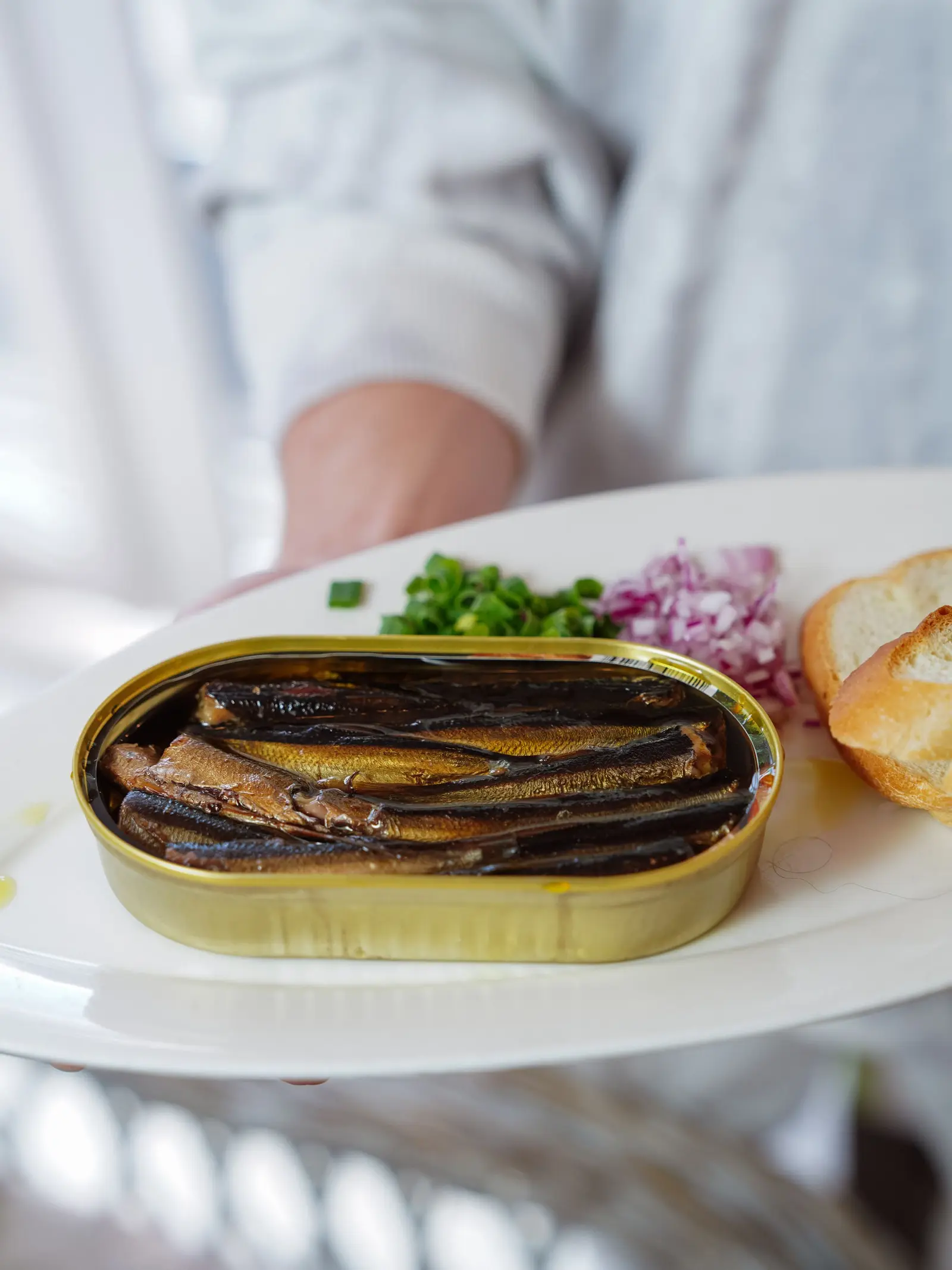 A gourmet plate of canned sardines served with greens and bread, plated as a delicacy