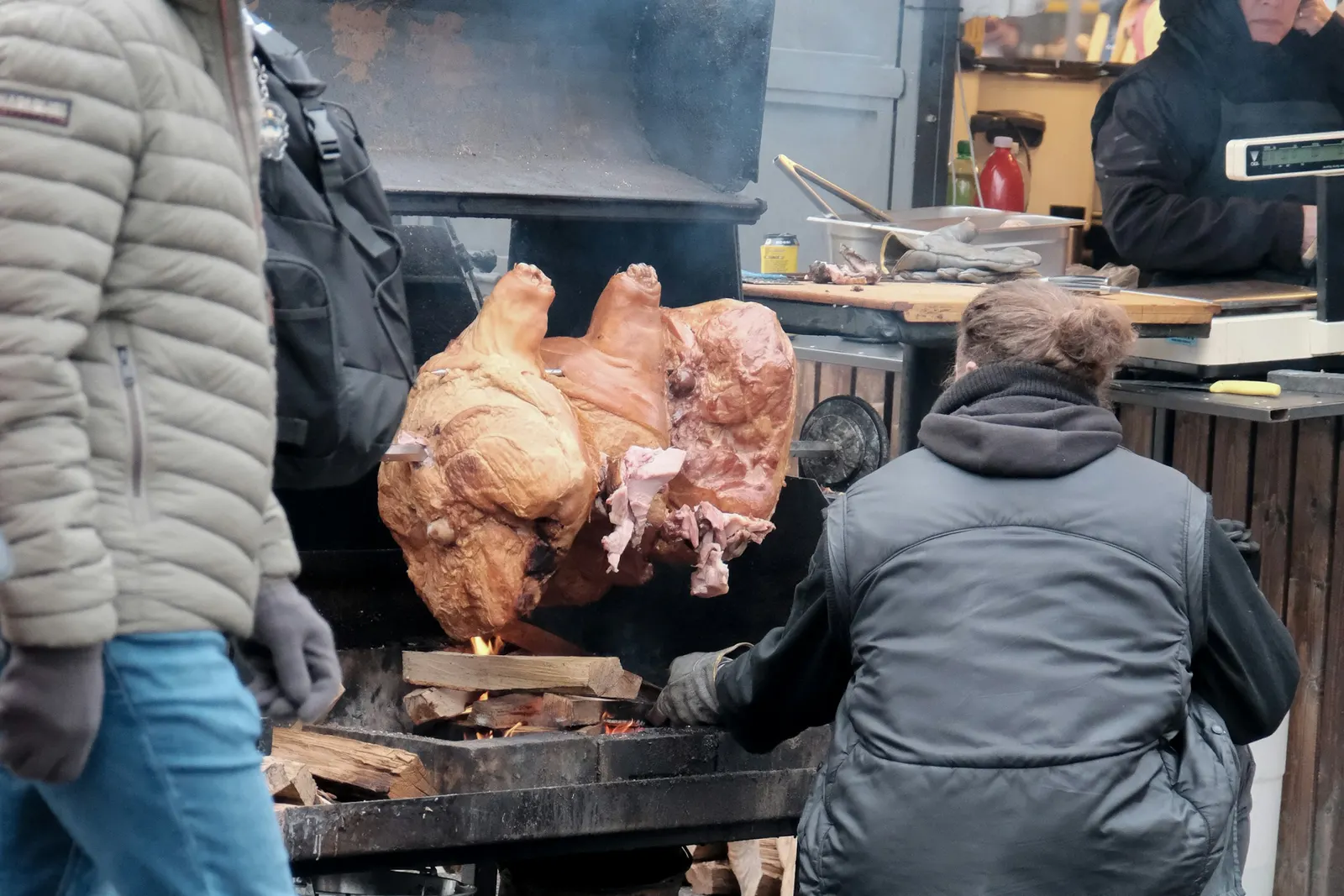Cooks tending a large cut of meat roasting over an open wood fire