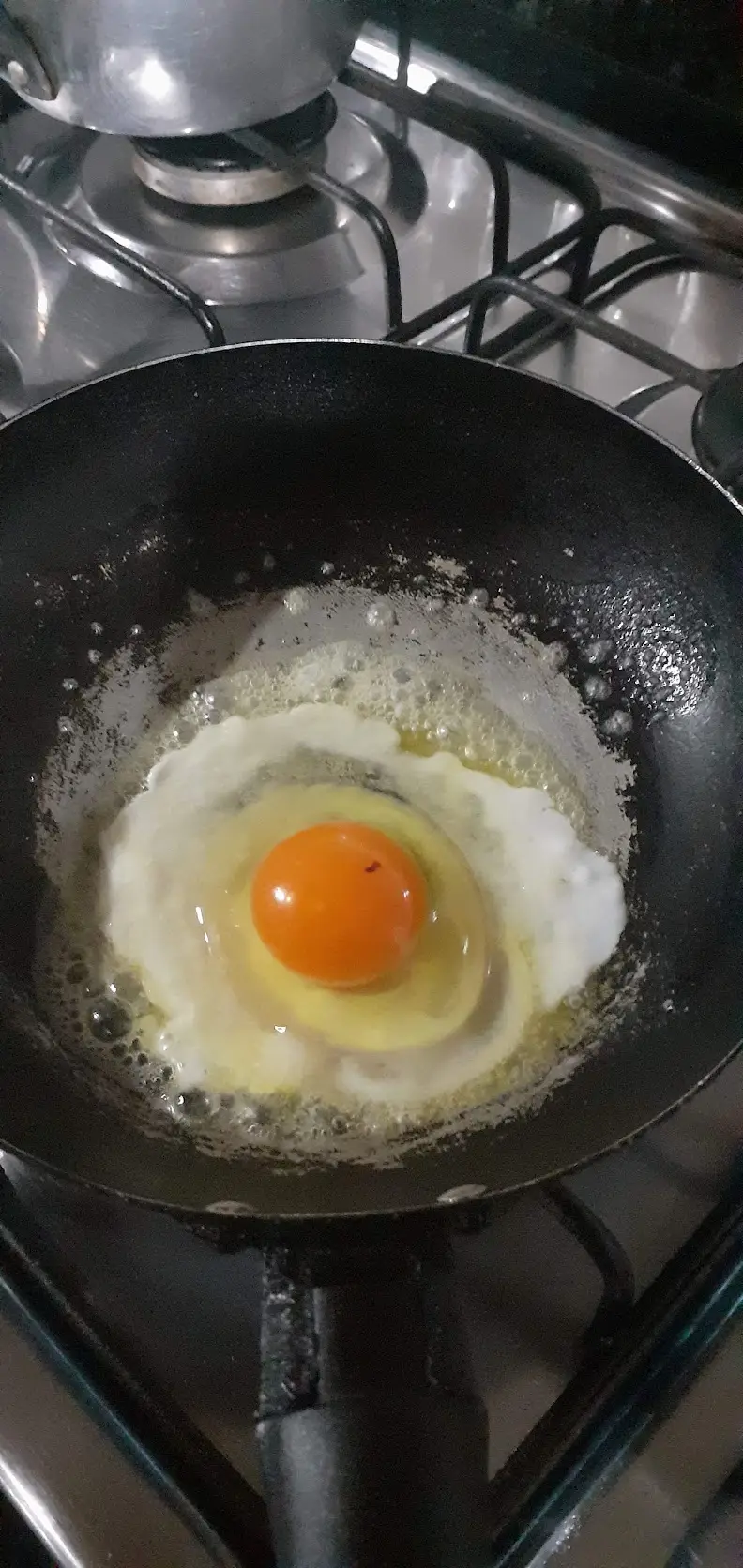 A young hen's first egg frying in a pan, its yolk a deep orange instead of pale yellow