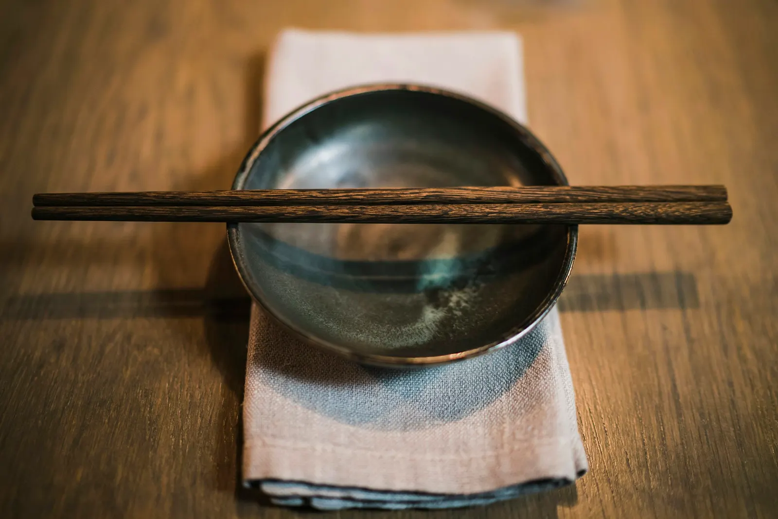 A pair of brown chopsticks resting on a round ceramic bowl on a wooden table