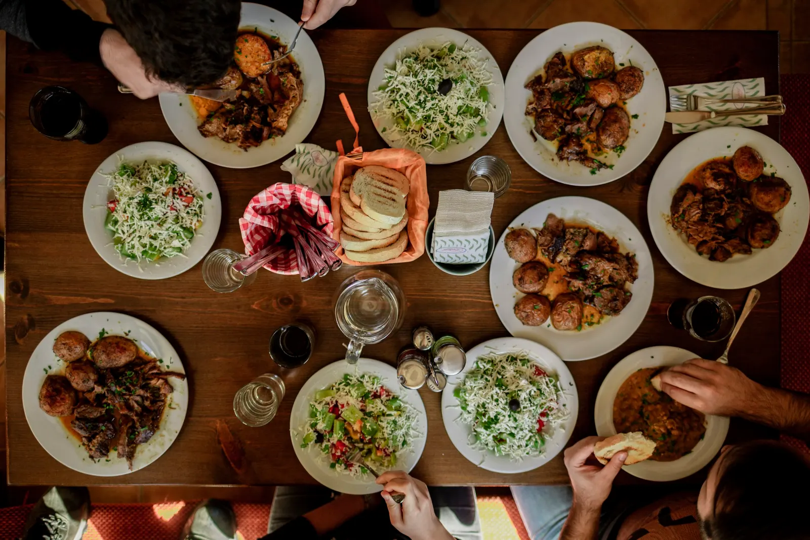 An overhead view of white plates filled with an assortment of shared dishes on a wooden table