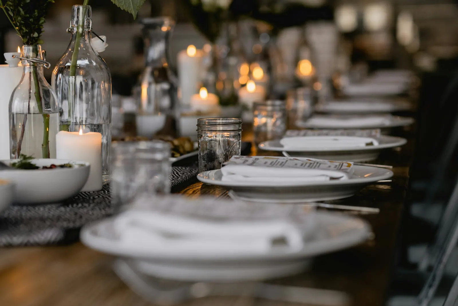 A formal place setting with white plates, candles, and arranged cutlery on a dark table