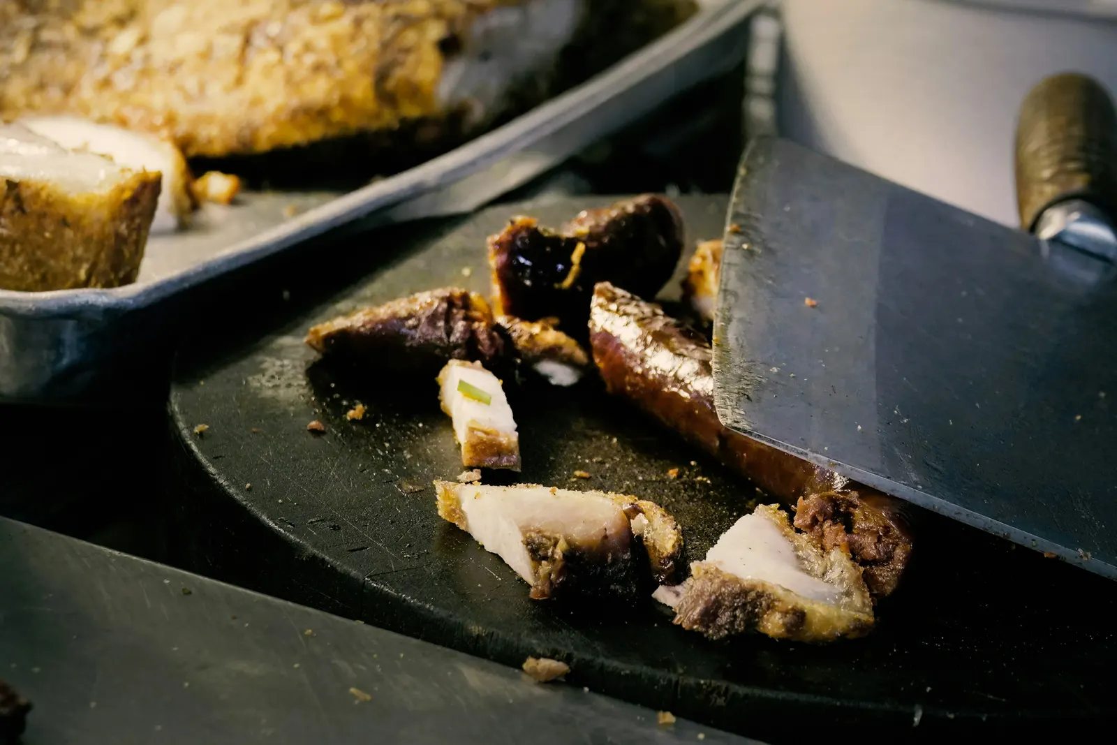 A cleaver chopping crisp-skinned roast lechón pork on a dark cutting board