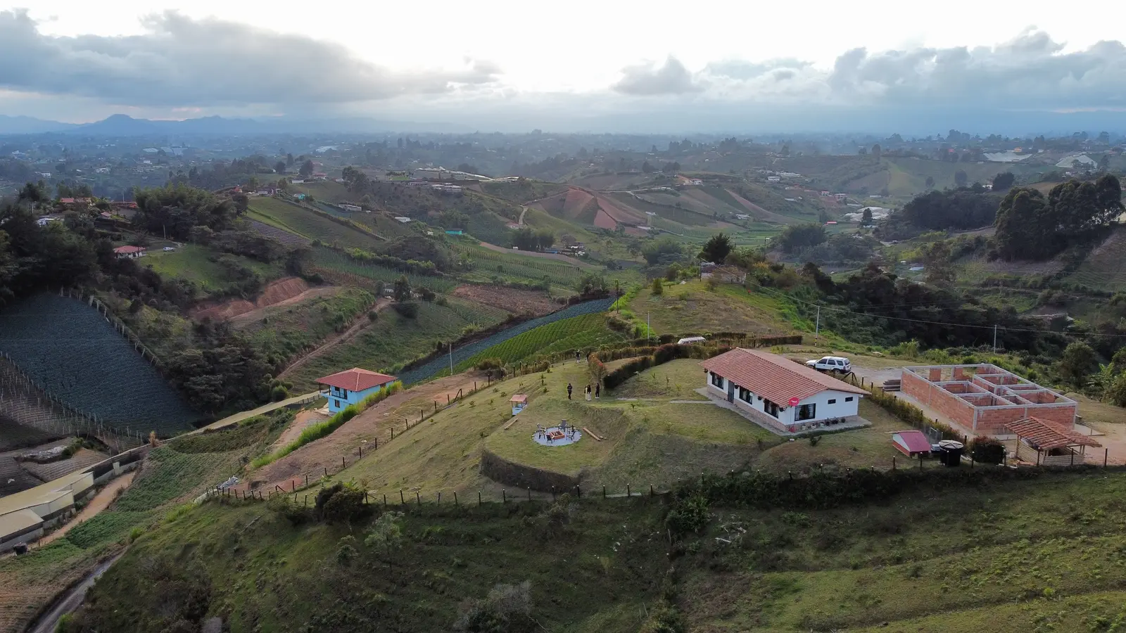 Aerial view of a hillside finca in Colombia, with a tiled-roof farmhouse and farmland terraced into green hills