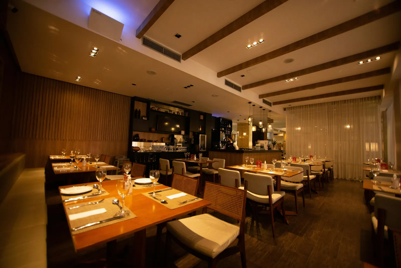 A set restaurant table with white linens, glasses, and place settings waiting for diners in a warm empty dining room
