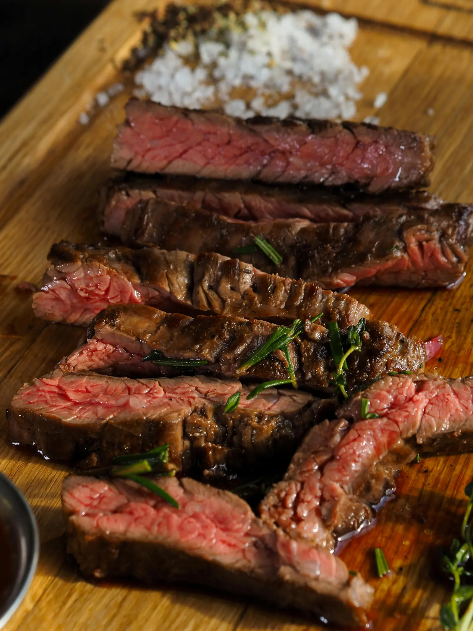 A sliced grilled steak on a wooden cutting board, the cross-section showing a pink medium-rare interior with a dark seasoned crust