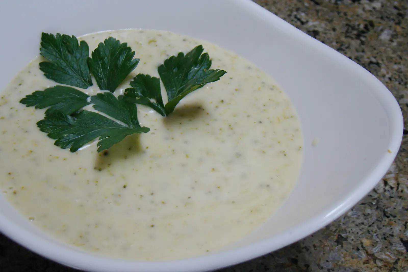 A bowl of smooth pale green pureed vegetable soup garnished with flat-leaf parsley, made without cream