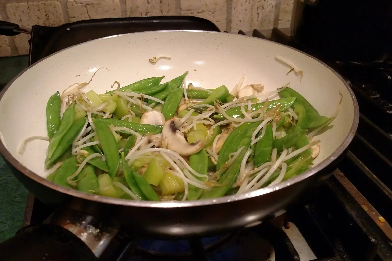 Green vegetables cooking in a single layer in a hot pan over an open flame, the method that keeps frozen vegetables from steaming