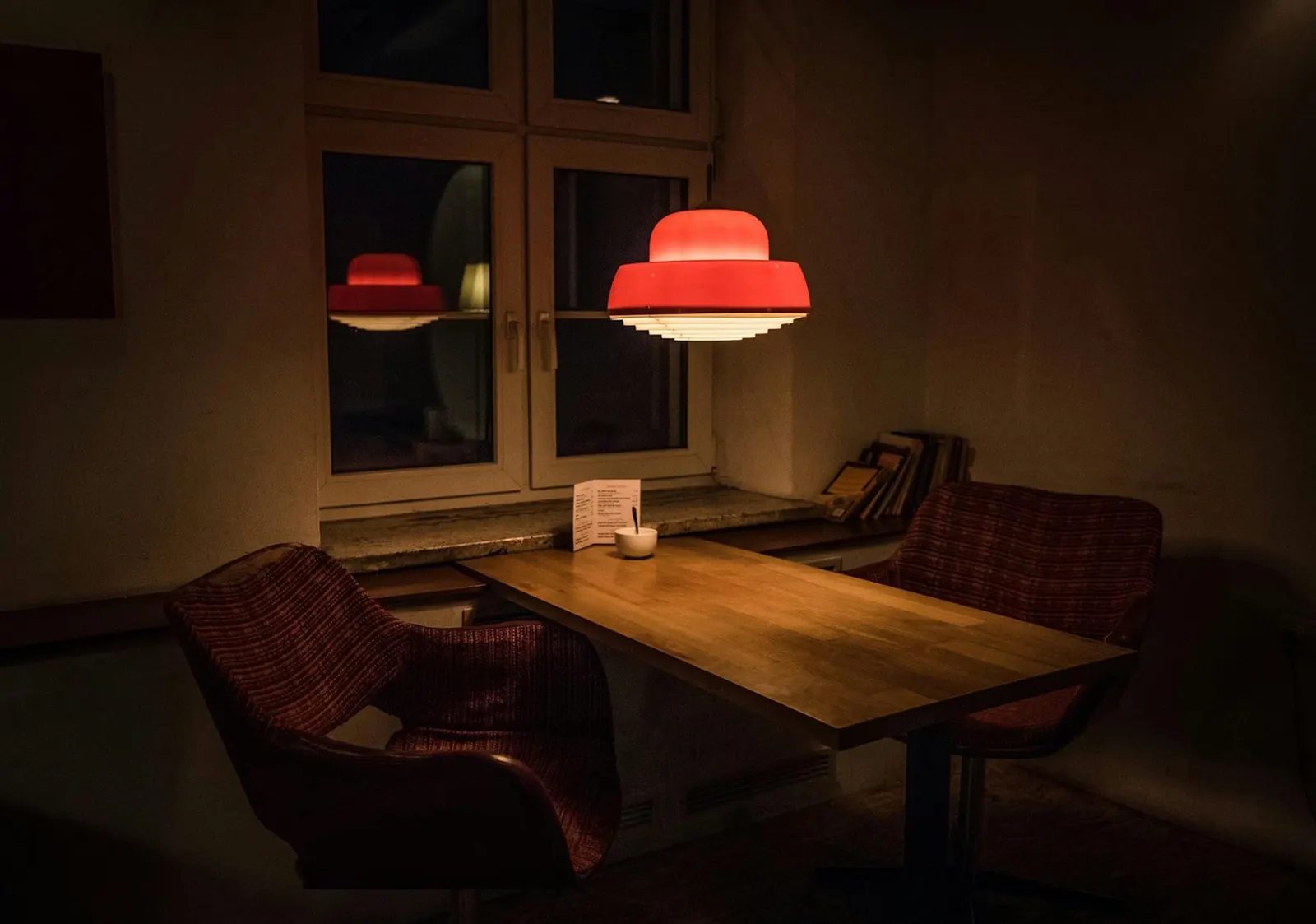 An empty restaurant interior in dim warm light at the end of service, an unoccupied table and chairs near a window