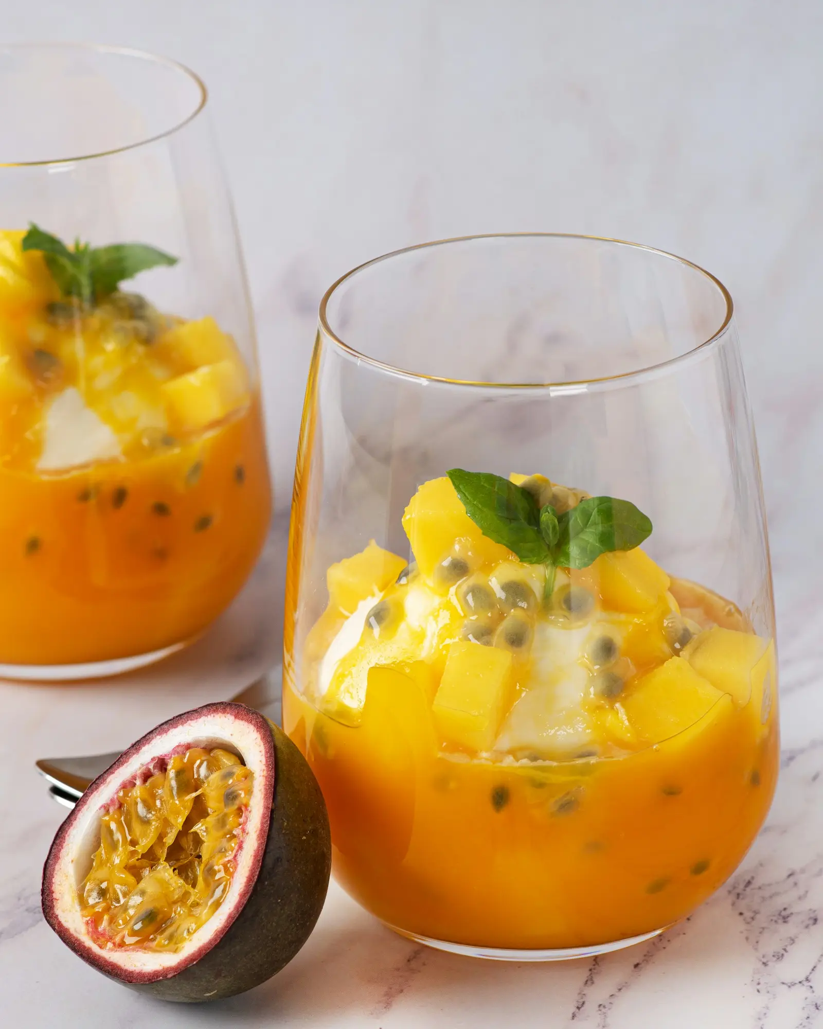 Passion fruit dessert in two glasses, mango and cream topped with fresh maracuyá pulp and mint