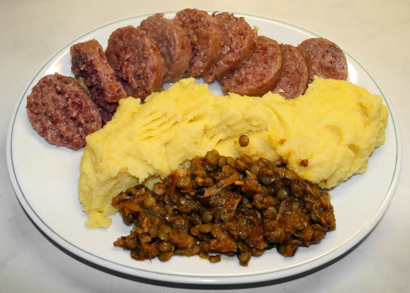 Sliced cotechino sausage served with lentils in sauce and polenta, the traditional Italian New Year's plate