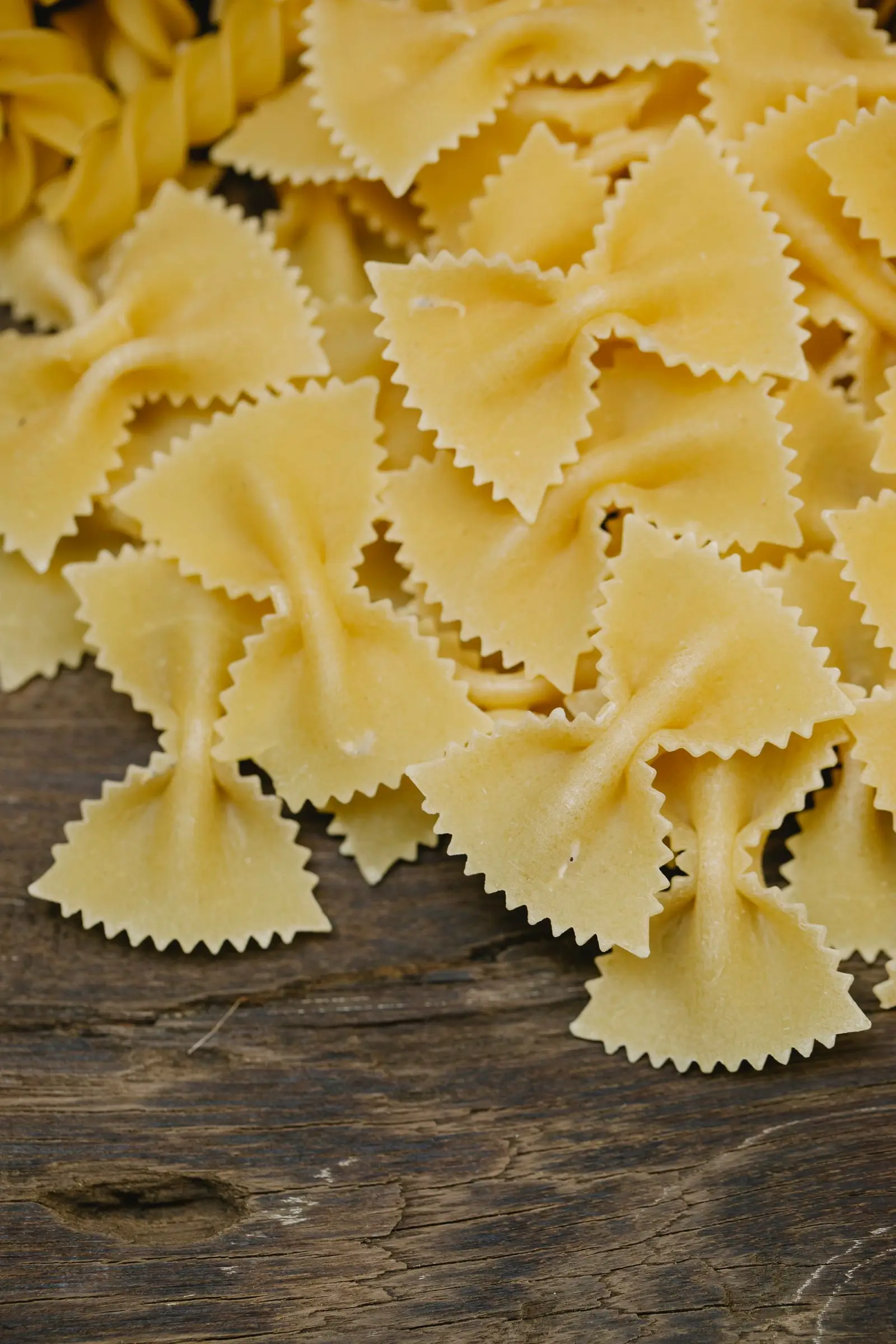 Uncooked farfalle bow-tie pasta with some fusilli spirals on a rustic wooden table