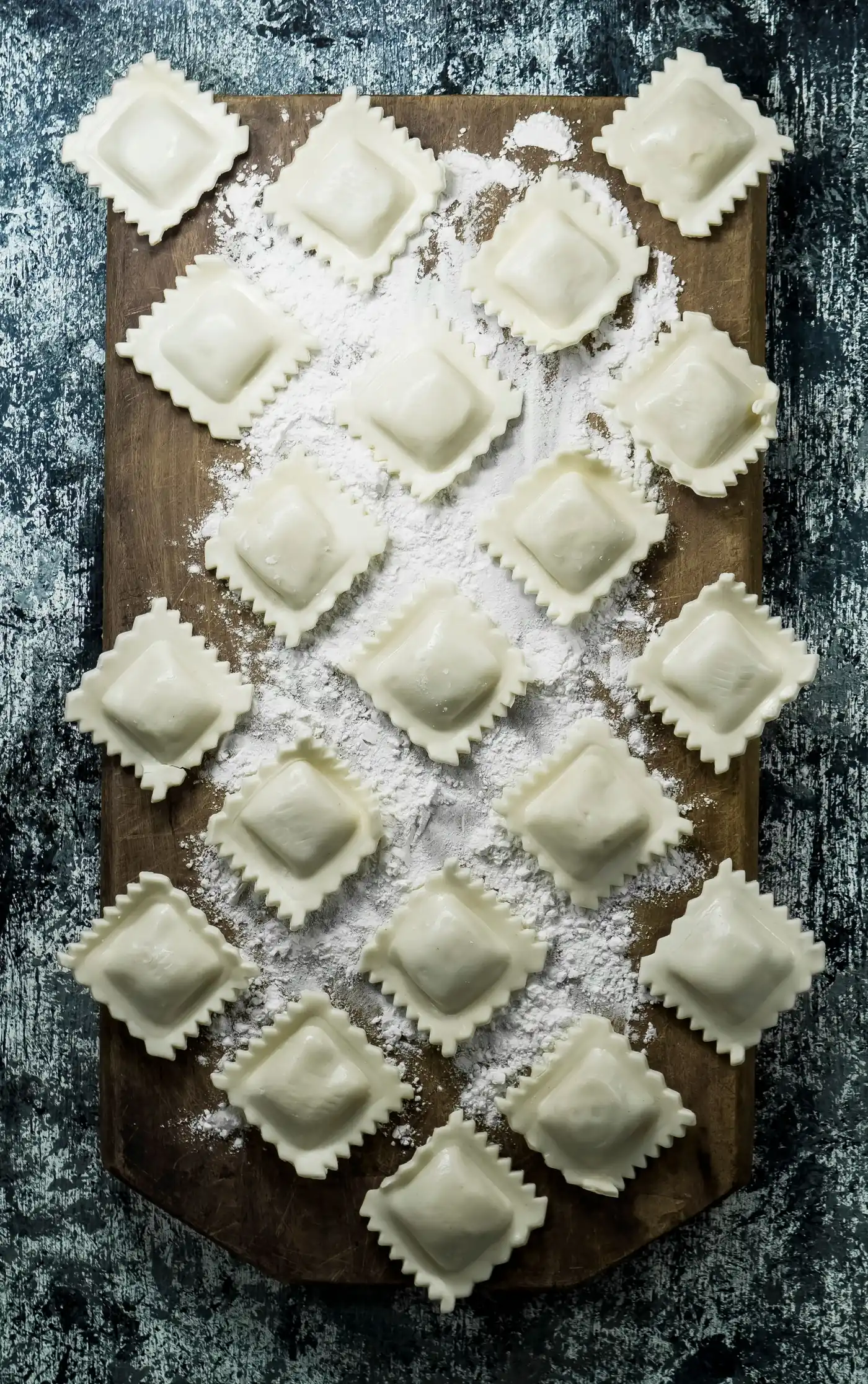 Rows of uncooked square ravioli dusted with flour on a wooden board