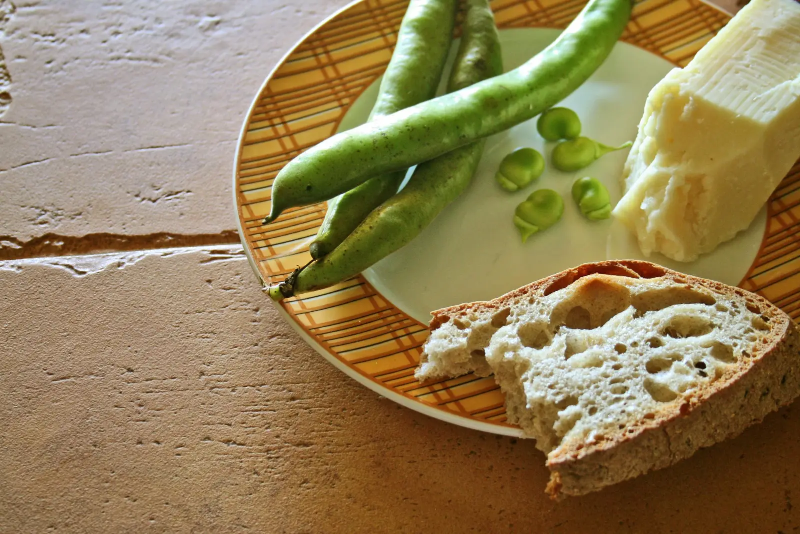 A wedge of young pecorino romano served as a table cheese with fresh fava beans and rustic bread
