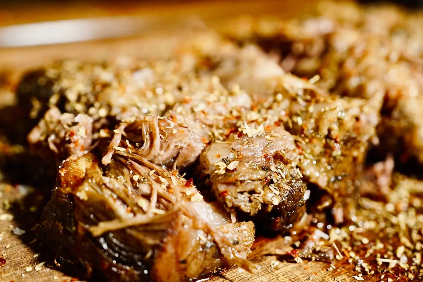 Shredded slow-cooked pork confit on a wooden board, glistening with fat and flecked with herbs