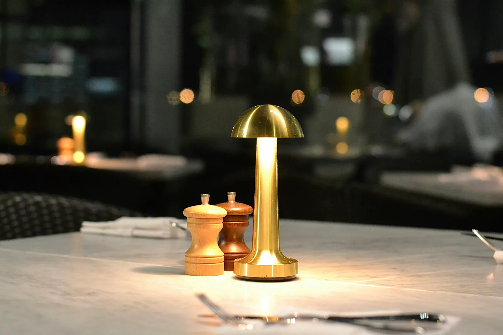 A restaurant table lit by a warm golden lamp, with plants and an upscale dining setting