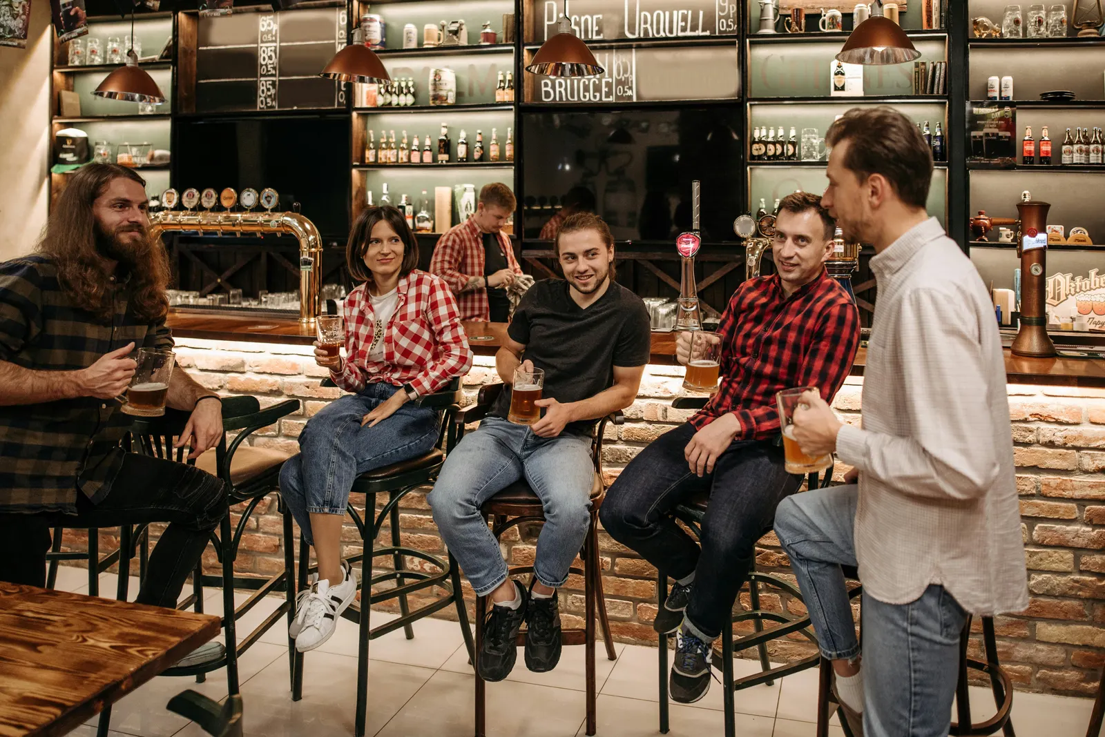 Friends talking and unwinding at a warm bar counter during happy hour, drinks and conversation in the soft amber light of early evening