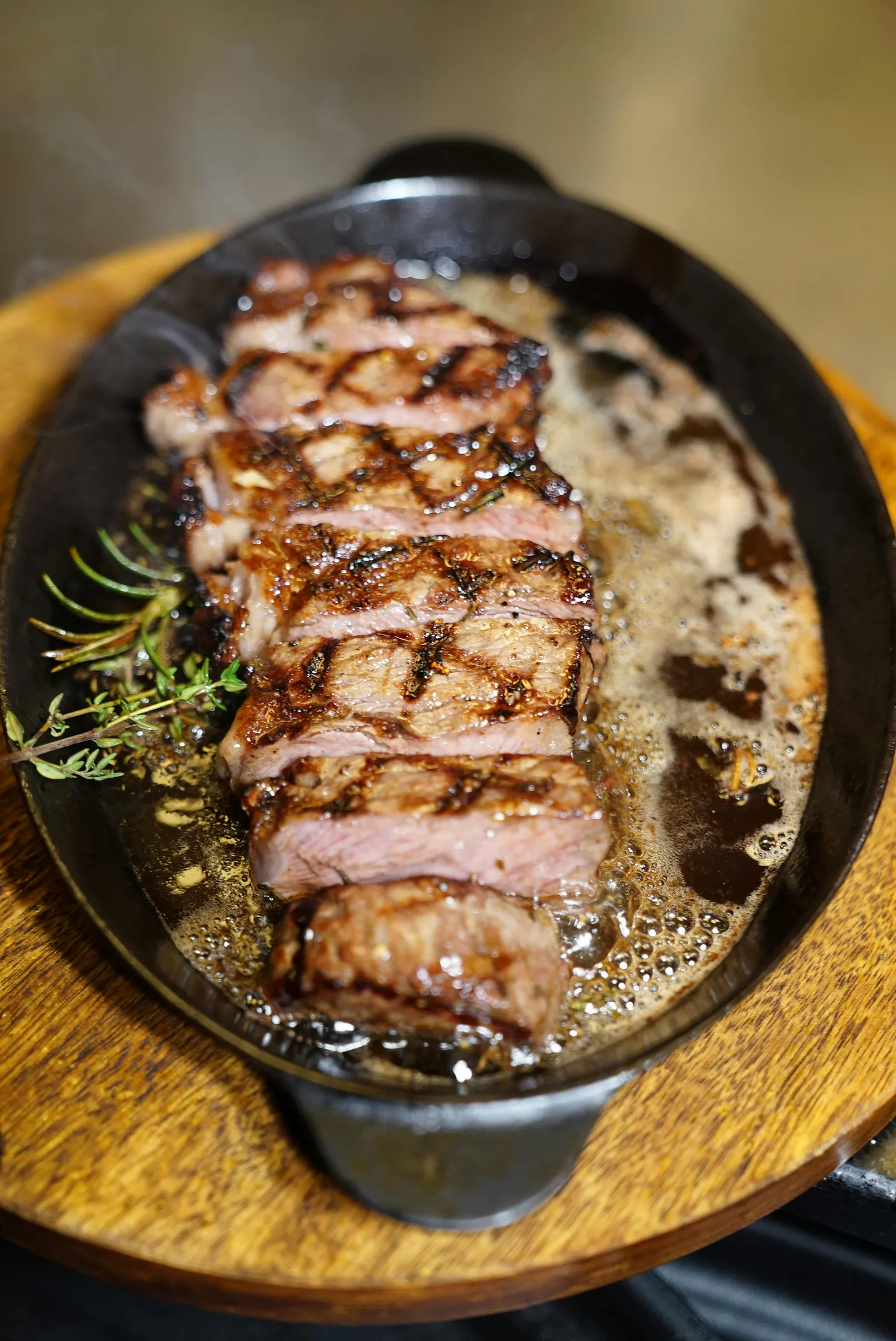 A juicy grilled steak garnished with fresh rosemary sizzling in a hot cast iron skillet, the crust deeply browned