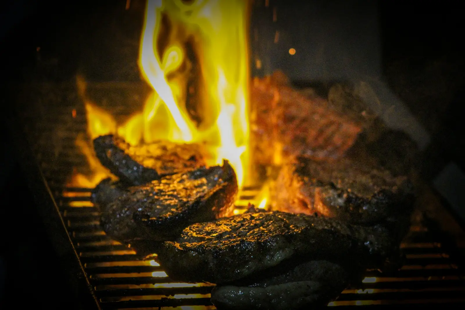 Steaks on a grill grate with a flame leaping up between them, a classic fat-fueled flare-up