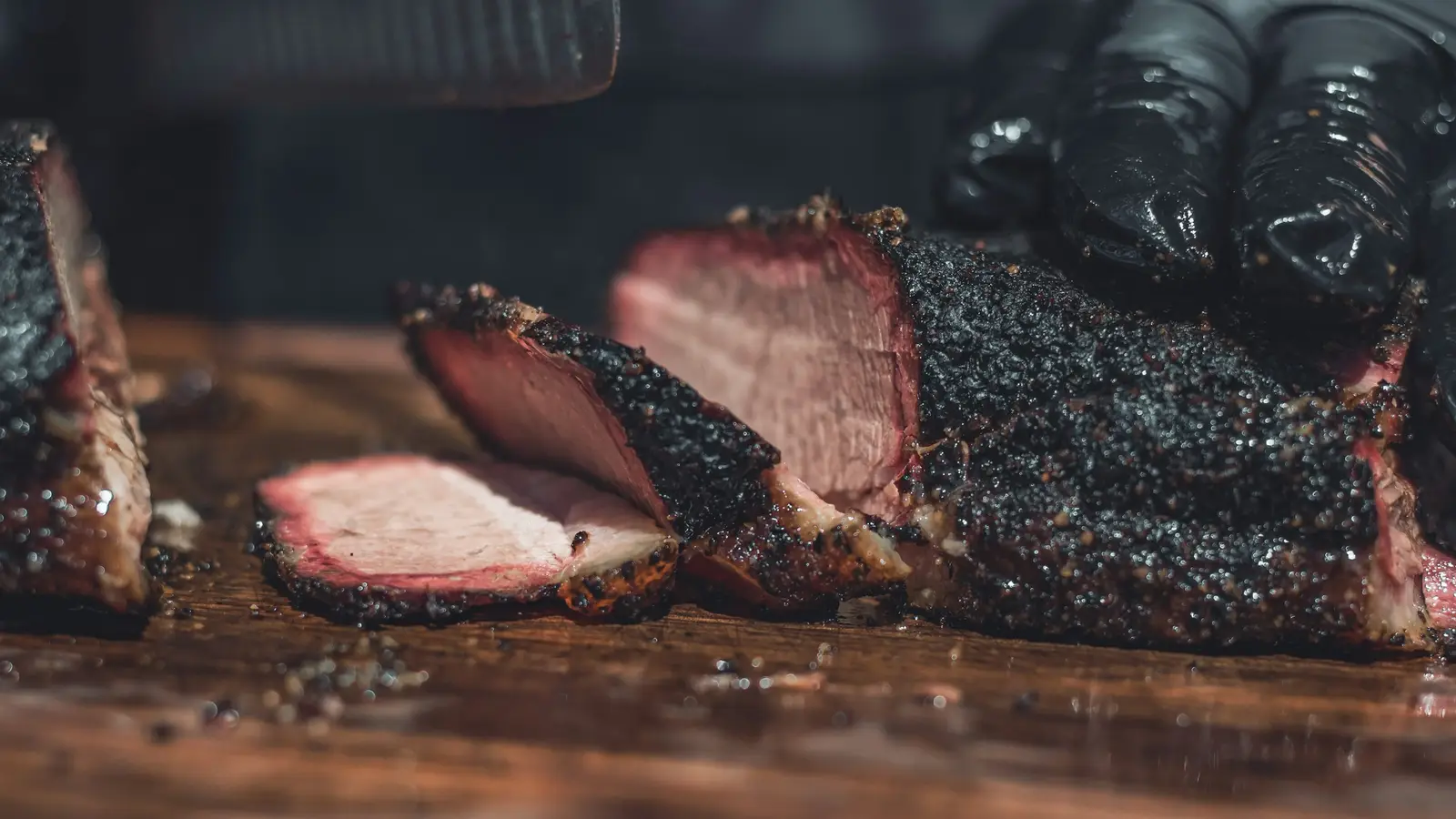 Slices of smoked brisket with a thick peppery bark and a visible pink smoke ring, resting on a wooden board