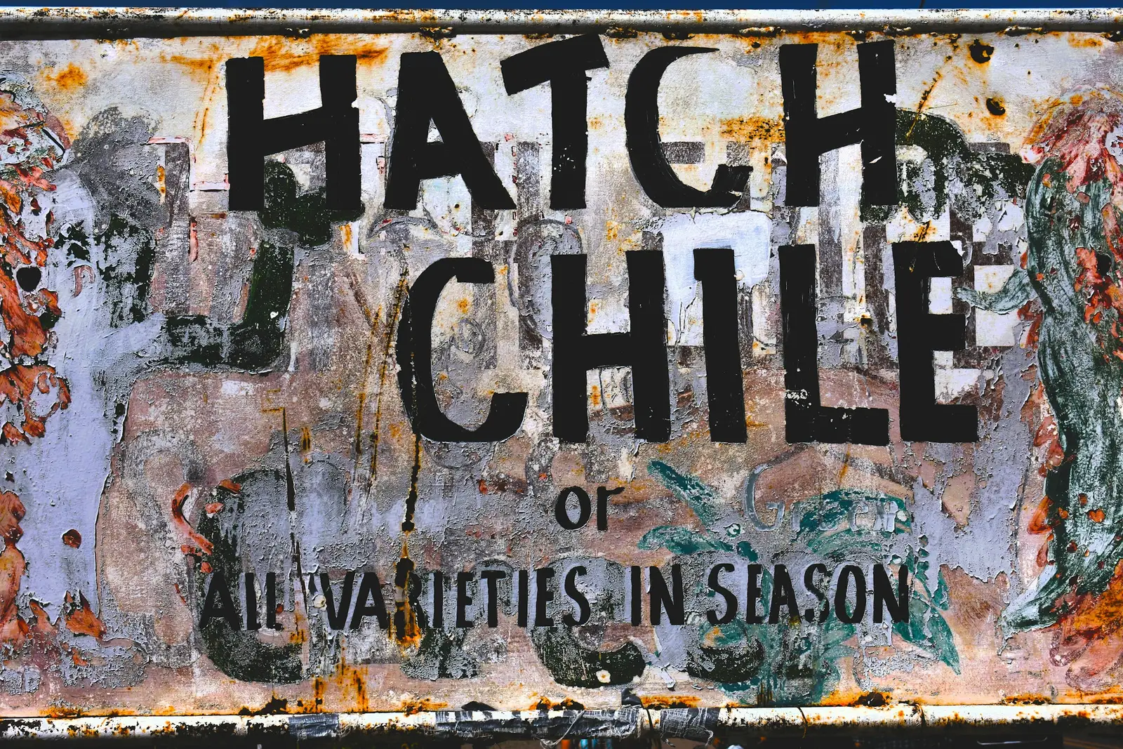 A weathered painted metal sign reading HATCH CHILE, all varieties in season, with rust across the surface