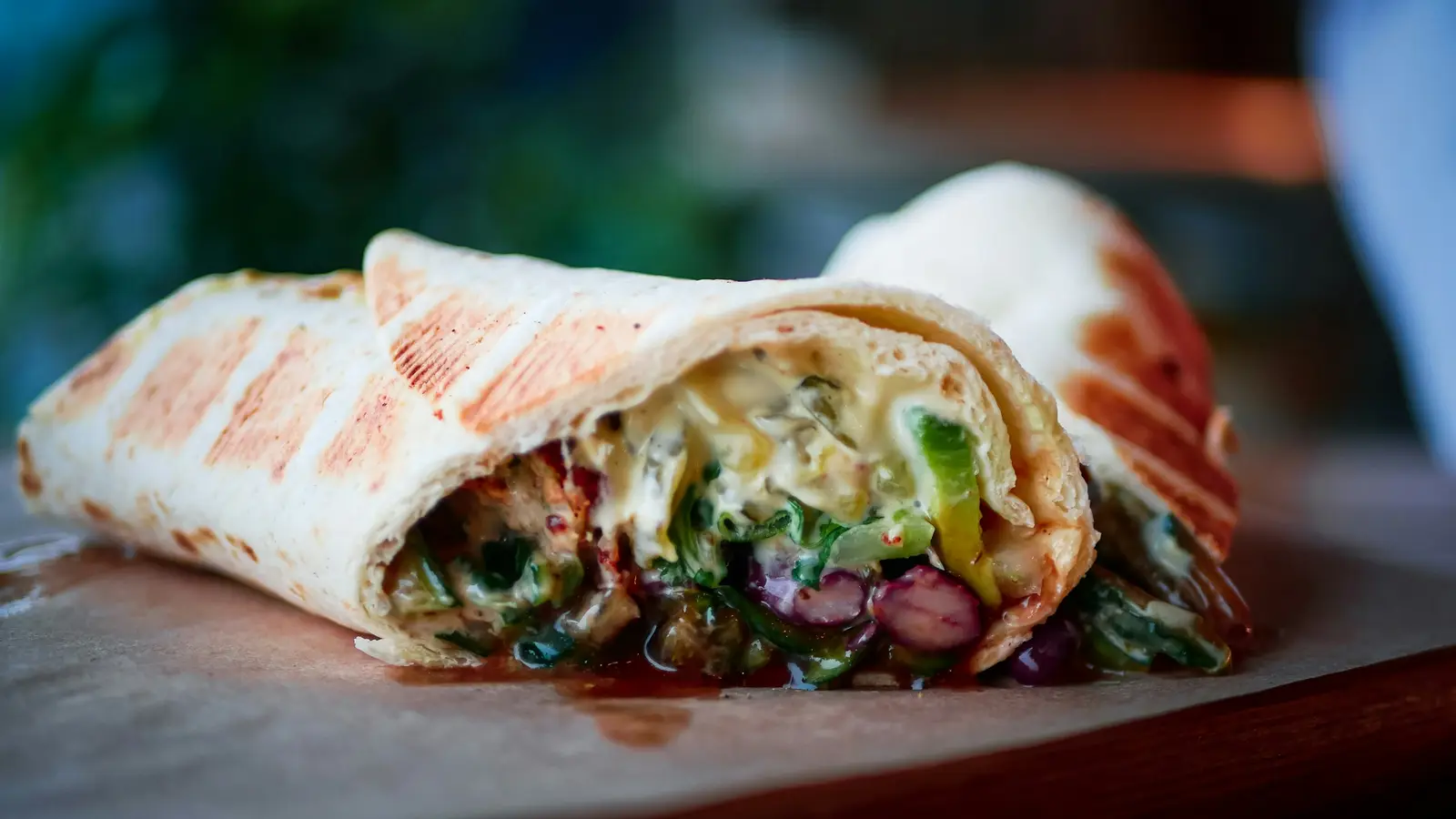 A shawarma wrap cut open to show layers of spit-roasted meat, pickles and sauce inside a grilled flatbread