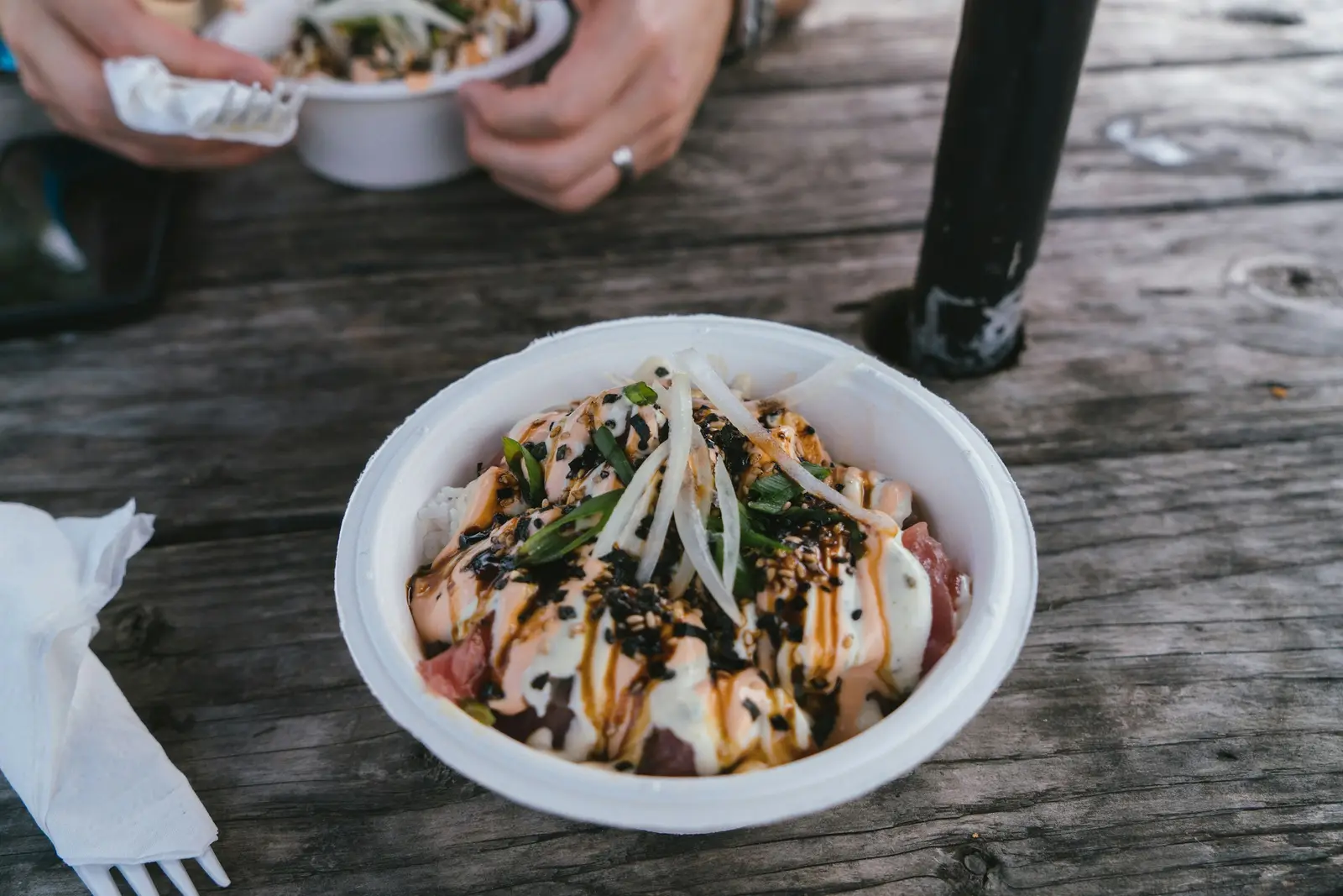 A poke bowl of cubed raw fish over rice with seaweed and green onion, on a weathered wooden table