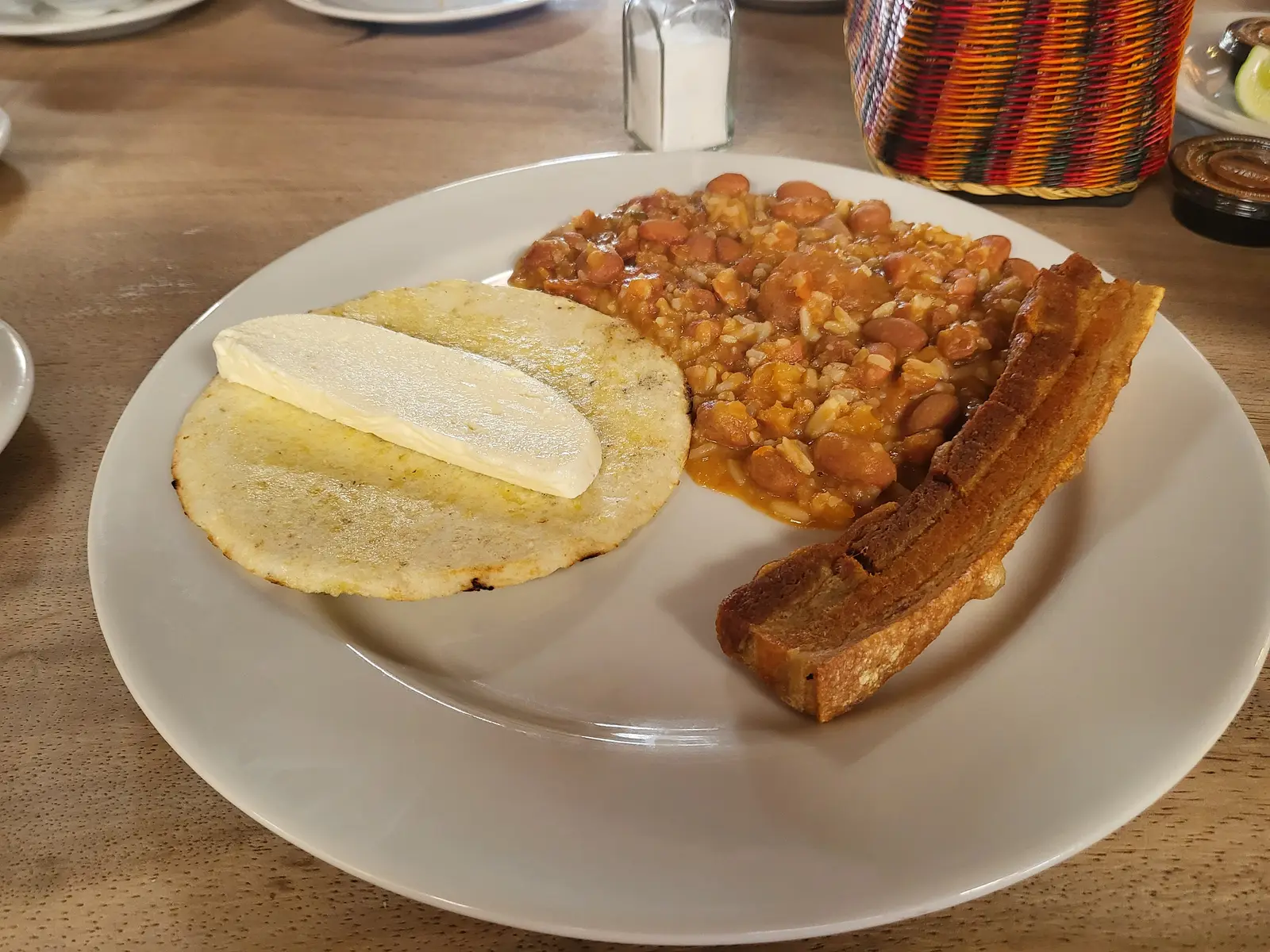 A paisa calentado breakfast: reheated rice and beans beside a grilled arepa topped with melting cheese and a strip of chicharrón