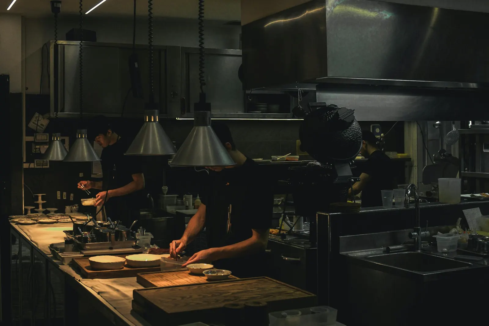 Three cooks working a restaurant line under heat lamps during dim service hours