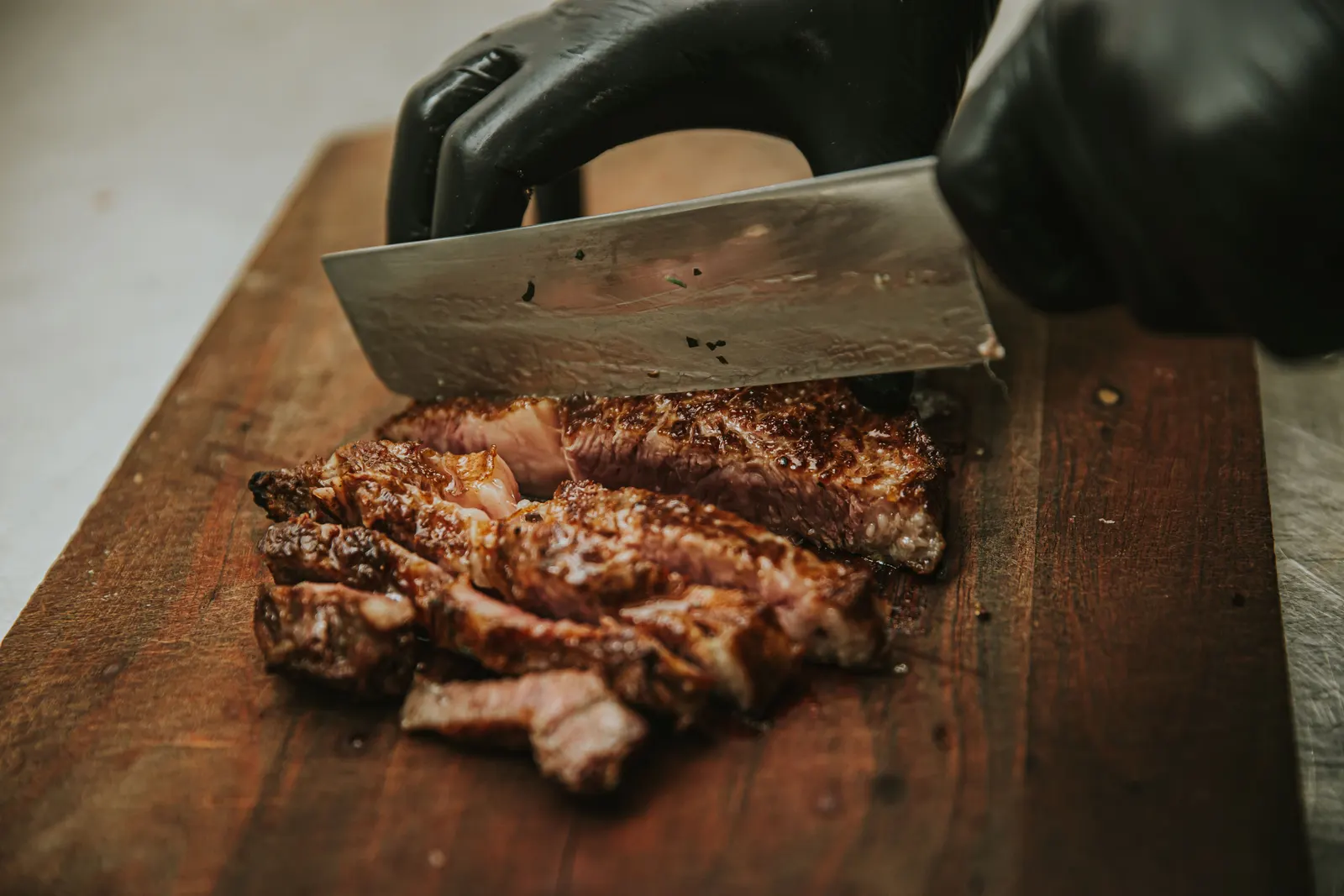 A butcher's hands cutting fresh beef with a heavy cleaver on a wooden counter, working a clean cut from a larger piece