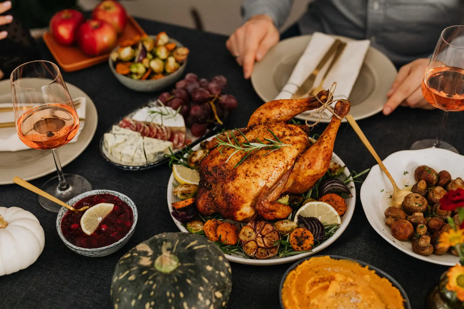 A crowded table of shared dishes including roast chicken, cranberry sauce, roasted mushrooms, cheese and grapes